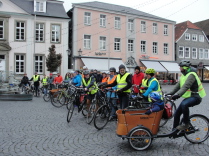 Foto Markplatz Lippstadt - Gruppe von ca. 15 mit bunten Warnwesten bekleidete Radfahrende stehen in einer Querreihe kurz vor dem Start der Critical Mass an ihren Rädern