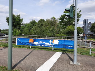 Mindestabstandsbanner des ADFC hängt an einem Geländergitter an der Kreiszung B55/Innenstadt in Warstein-Belecke