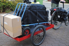 Ein Fahrrad mit Sattetaschen und Anhänger. Darauf eine Sackkarre, ein großer Karton und der im Transportsack steckende ADFC Pavillon