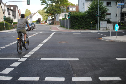 Ein Fahrradfahrer in Rückenansicht bei der Querung des Kölner Rings entlang der Kreuzung Paradieser Weg.