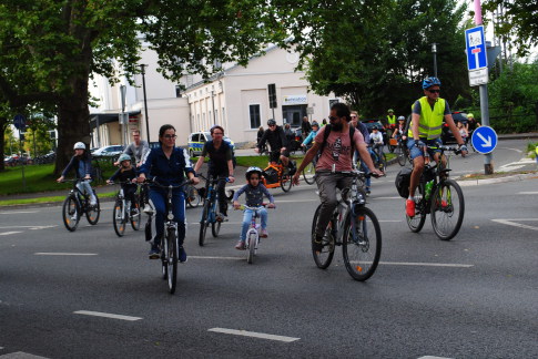 Im Vordergrund eine Familie mit einem kleinen Kind auf dem Rad, daneben ein Ordner mit Sicherheitsweste dahinter eine bunte Schar von radfahrenden Kindern und Erwachsenen mit Lastenrädern oder Solorädern