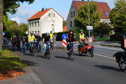 Eine Gruppe radfahrender mit Helmen und Schutzwesten von kleinen und großen Rädern nimmt eine ganze Spur in Fahrichtung ein