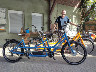 blaues und oranges Schauff E-Tandem mit J. Schauff im Hintergrund